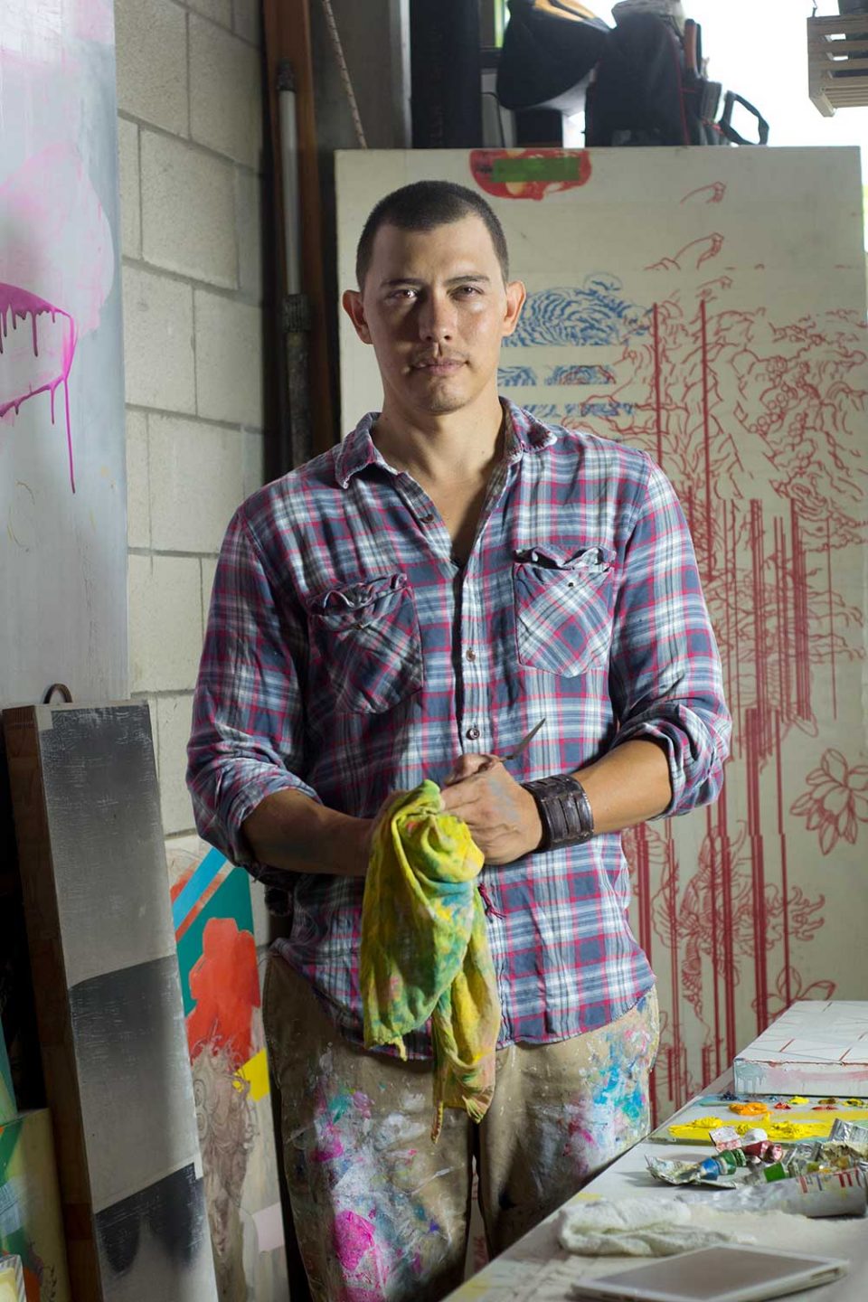Kalani Largusa with paint covered smock in front of one of his works