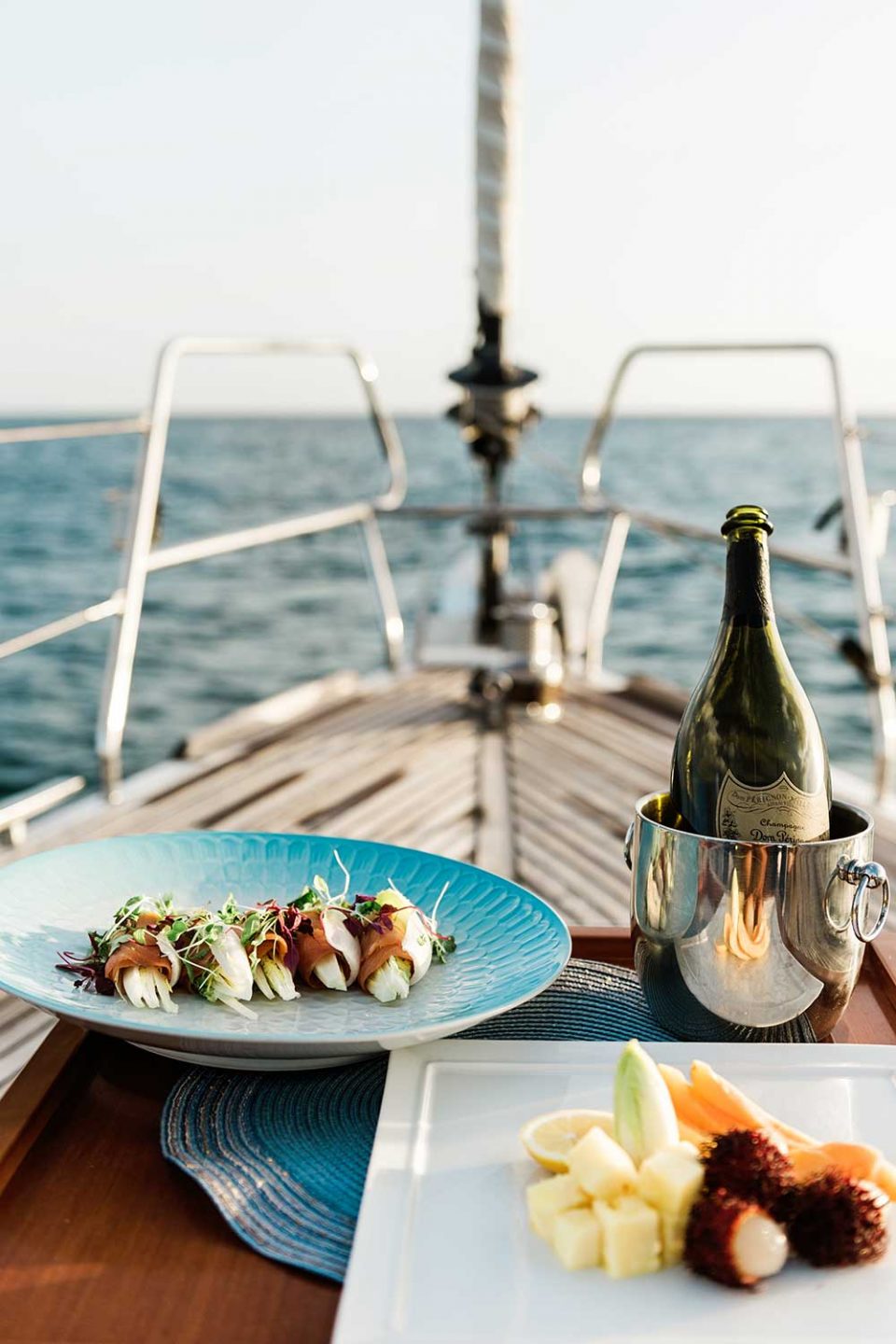 view of sushi plate, wine bottle and fruit plate on deck of yacht overlooking the ocean