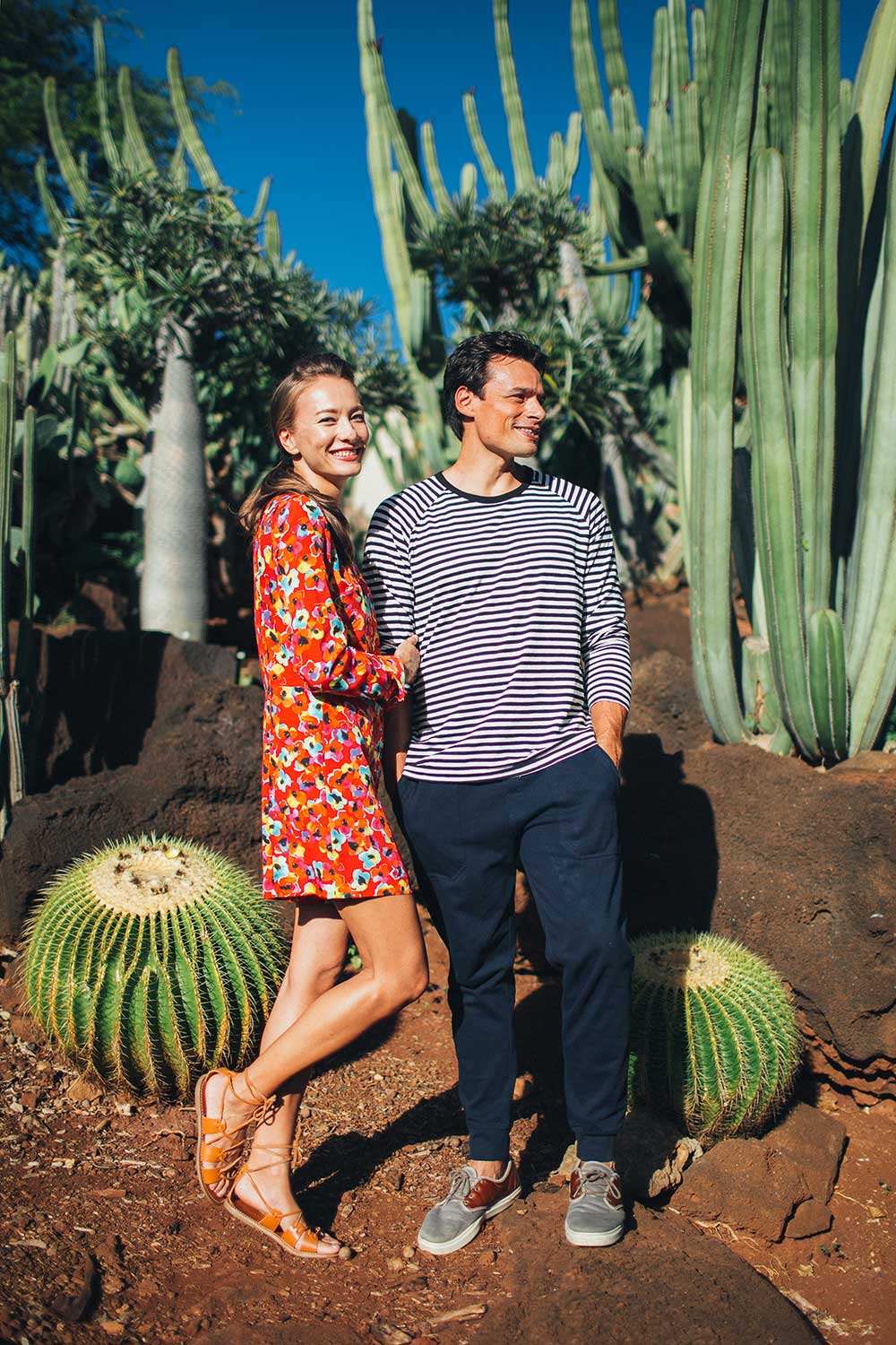 Woman in red flowered dress holding man's arm standing in cactus garden