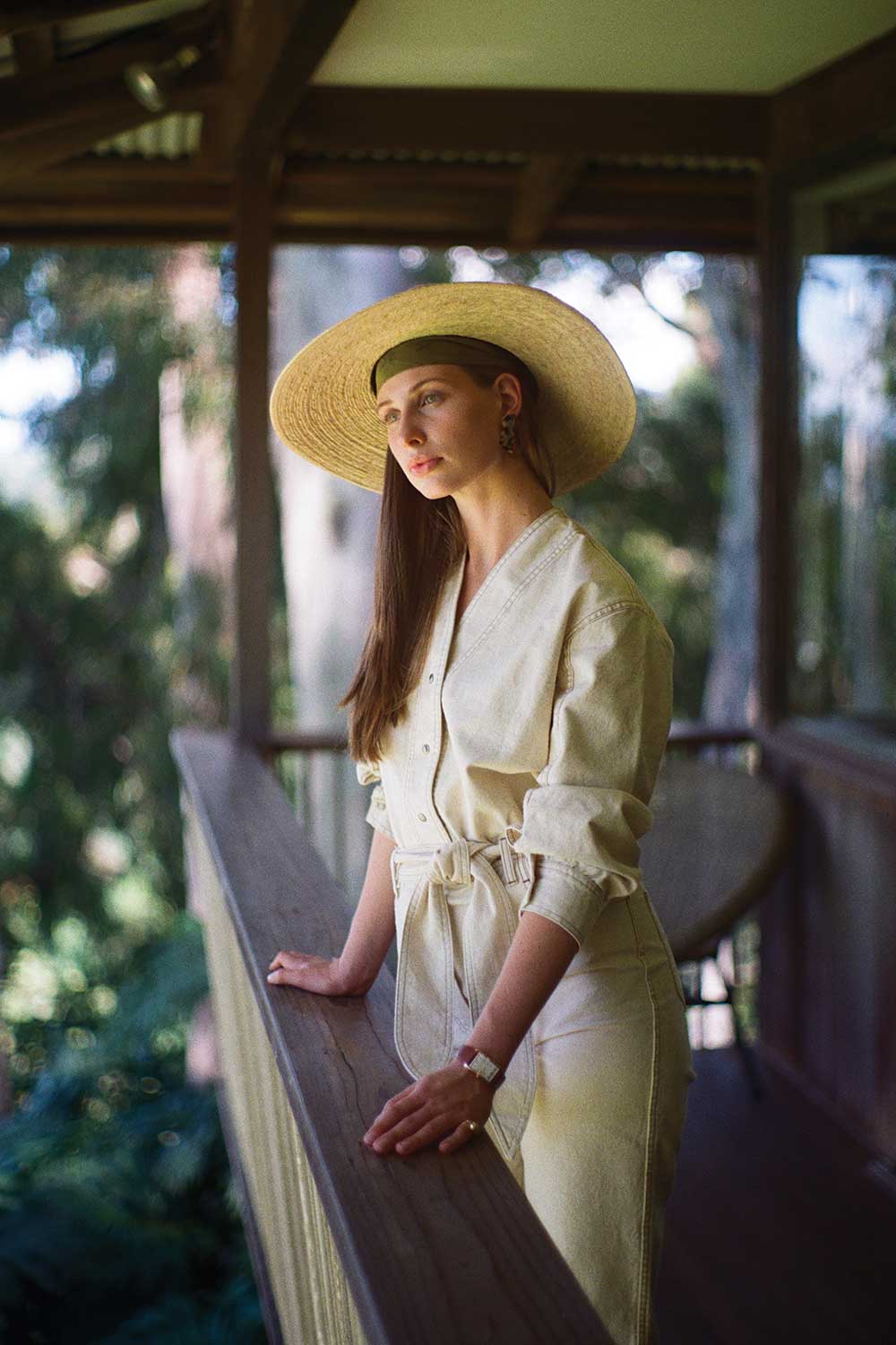 Woman gazing into distance wearing hat and cream denim jumpsuit