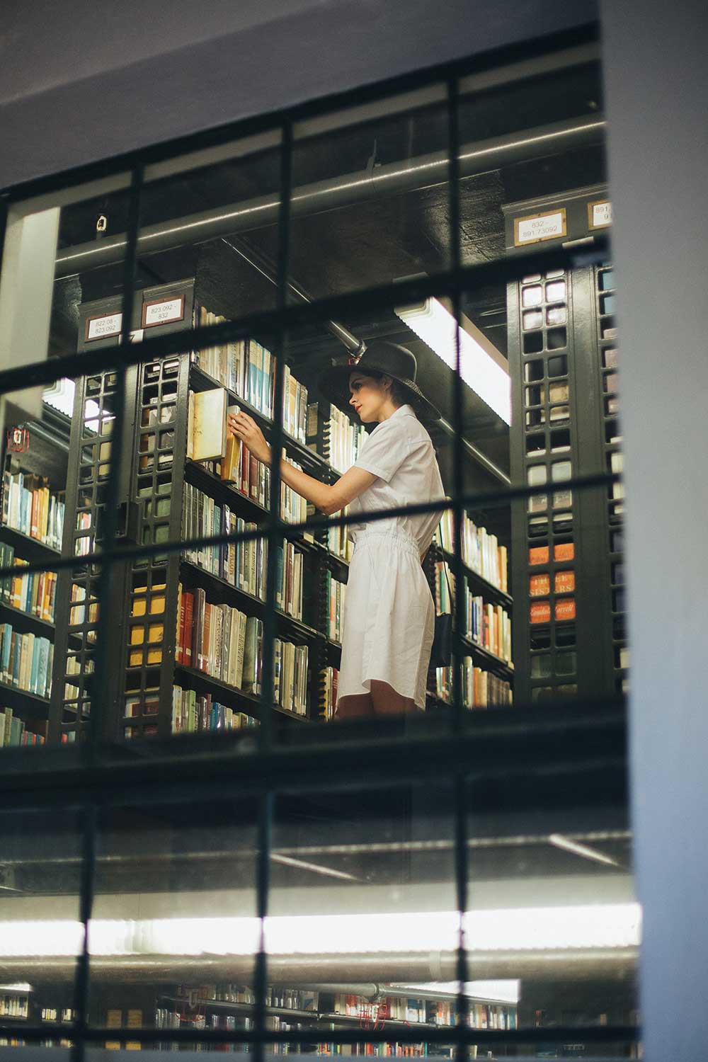 Woman in black hat and white dress looking through books at a library