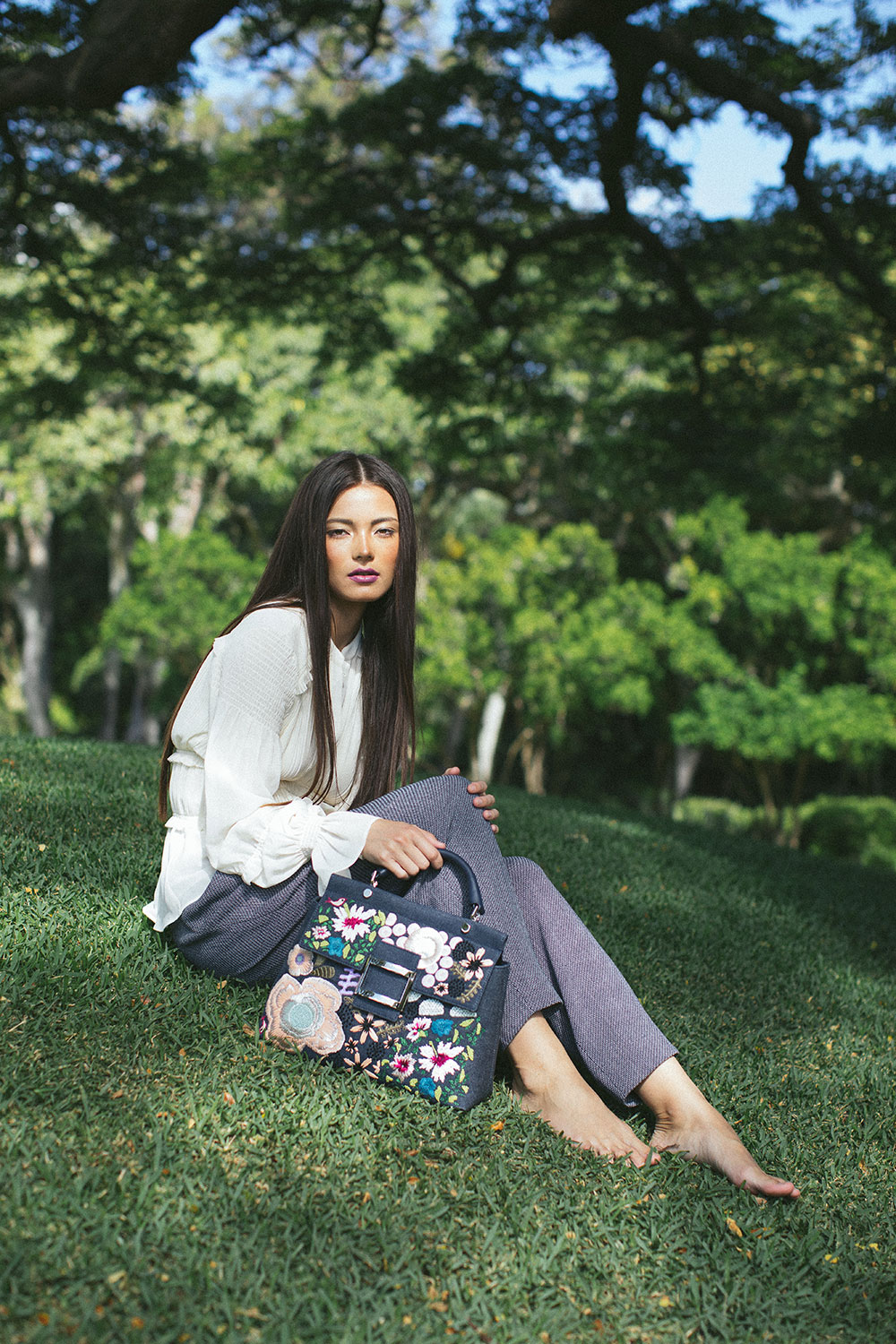 Model sitting in grass with denim handbag