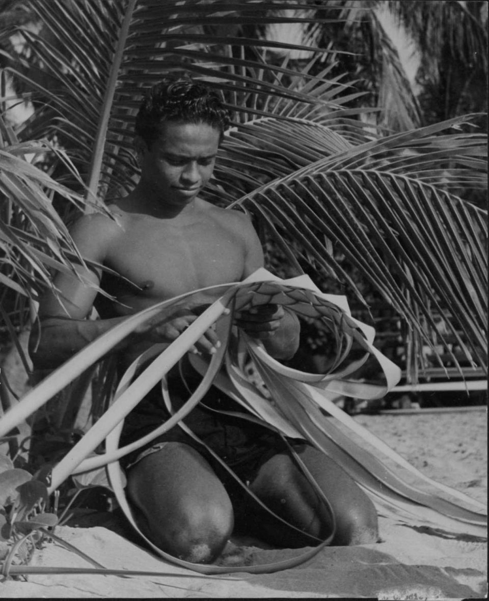 Black and white developed image of man weaving with coconut leaves.