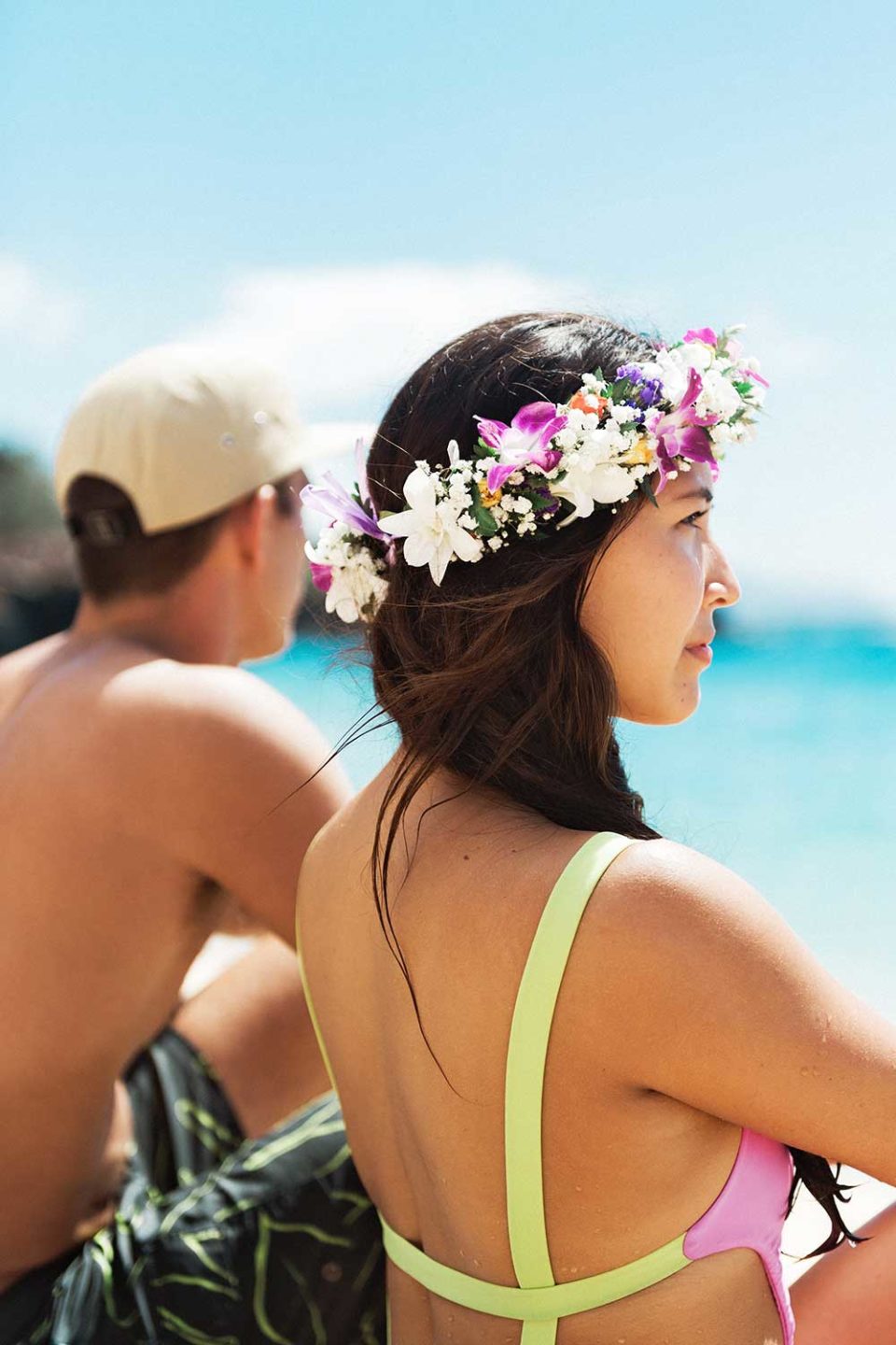 Woman with lei in hair and man sitting near ocean